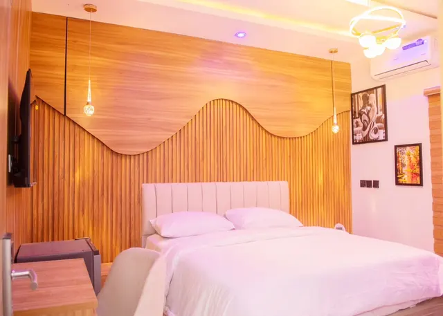 Executive Room with a wave-shaped wood-slat feature wall, cream upholstered bed, pendant lights and a wall-mounted TV
