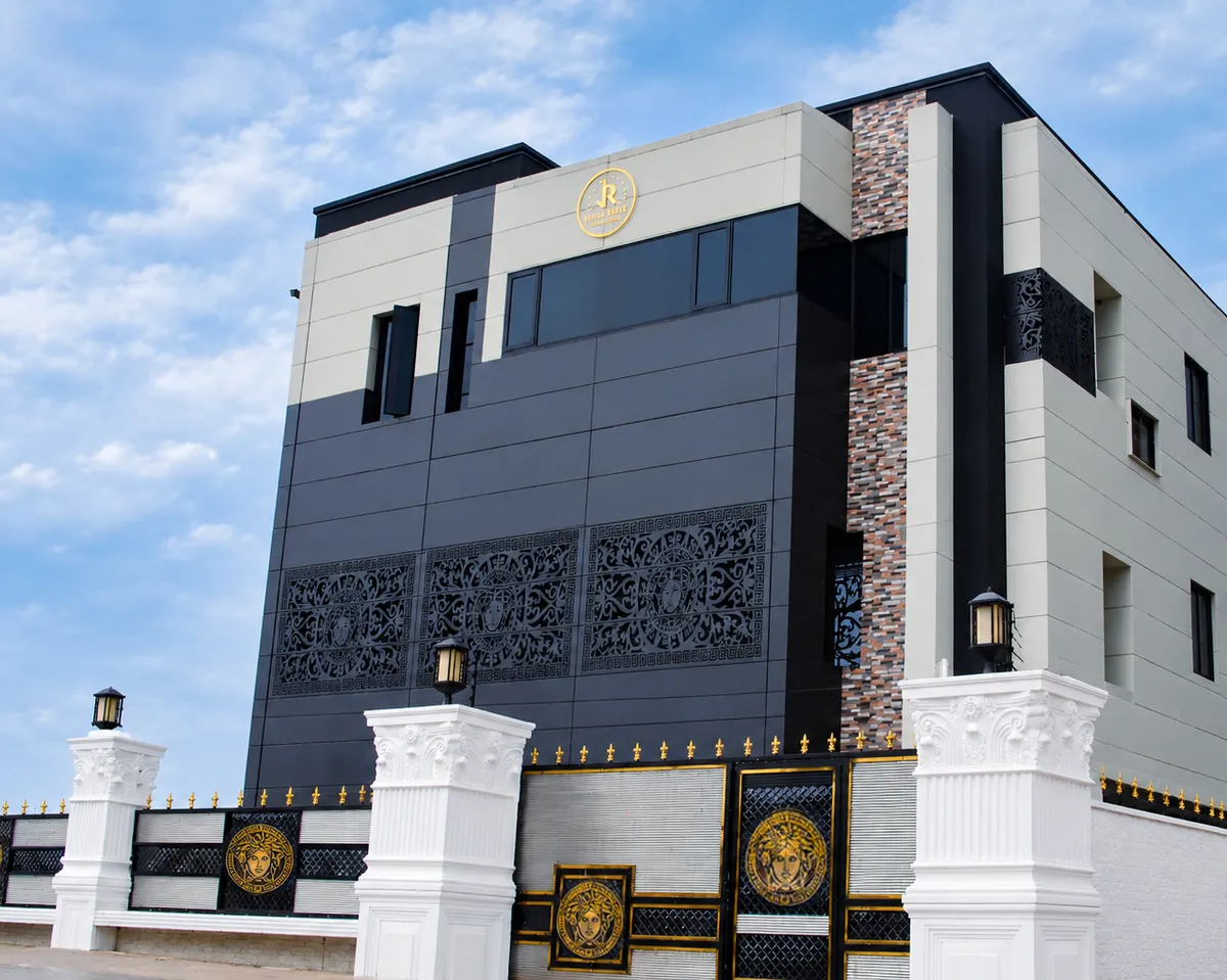 Juls & Riff Lagos from the side under a blue sky, with dark and cream cladding, carved decorative screens, a gold emblem and white gate pillars