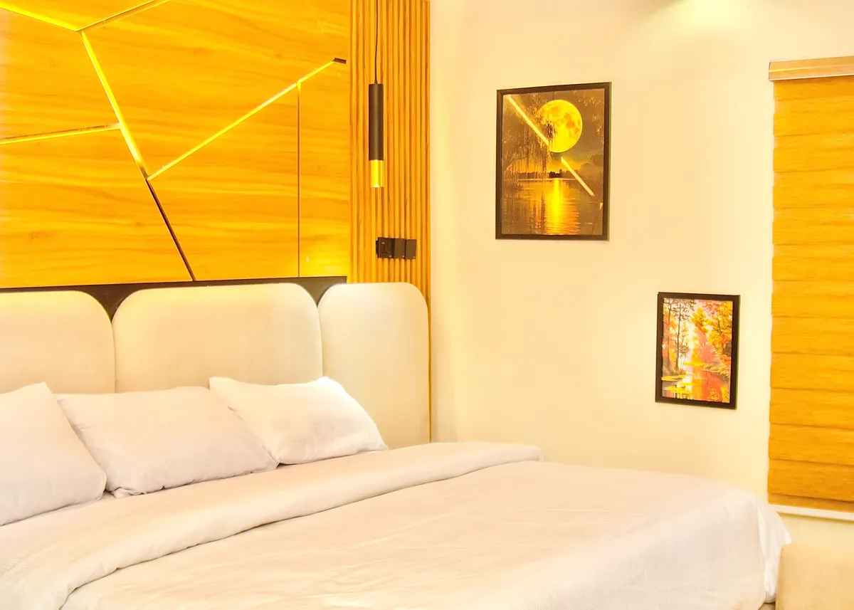 Guest room with a lit geometric wood-panel wall, cream upholstered bed and framed artwork