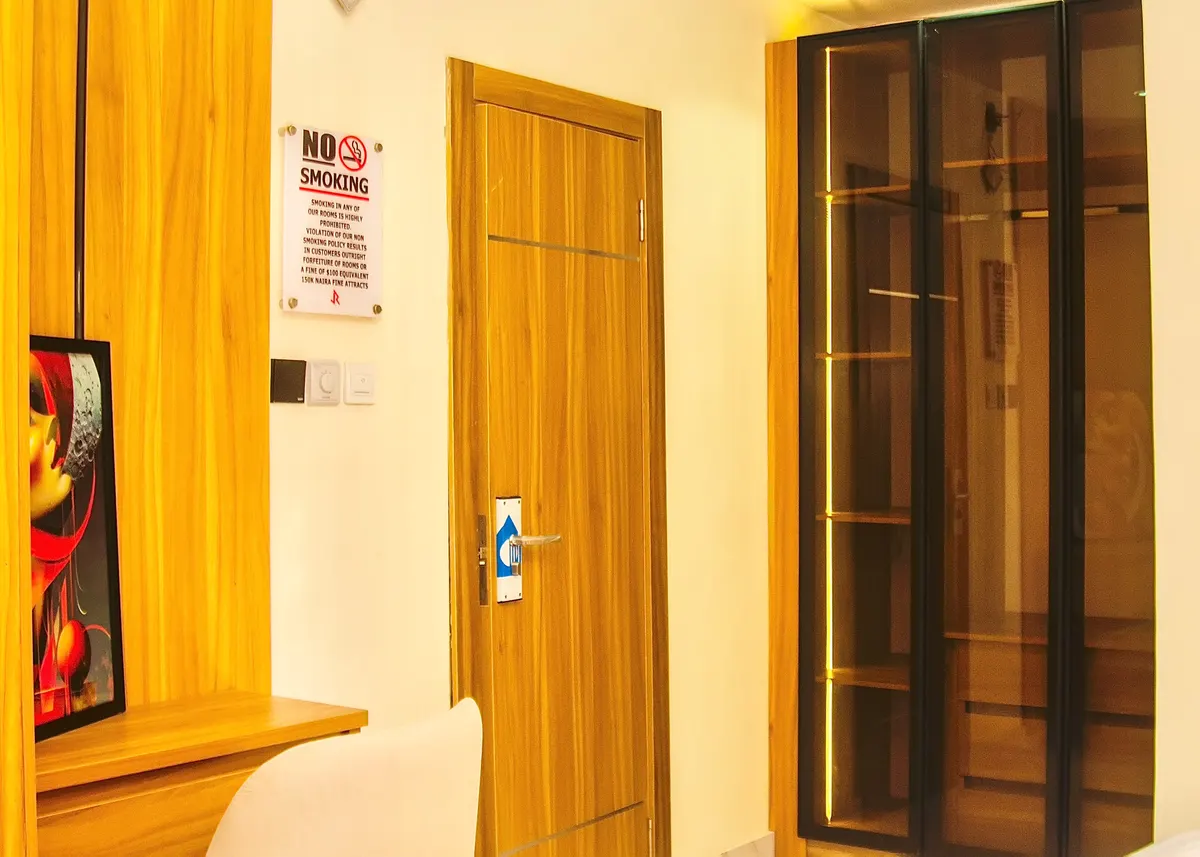 Guest room interior with a wooden door, glass-fronted wardrobe and a no-smoking sign