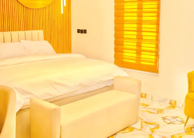Standard Room bed with white bedding, upholstered headboard and bench beside a window blind
